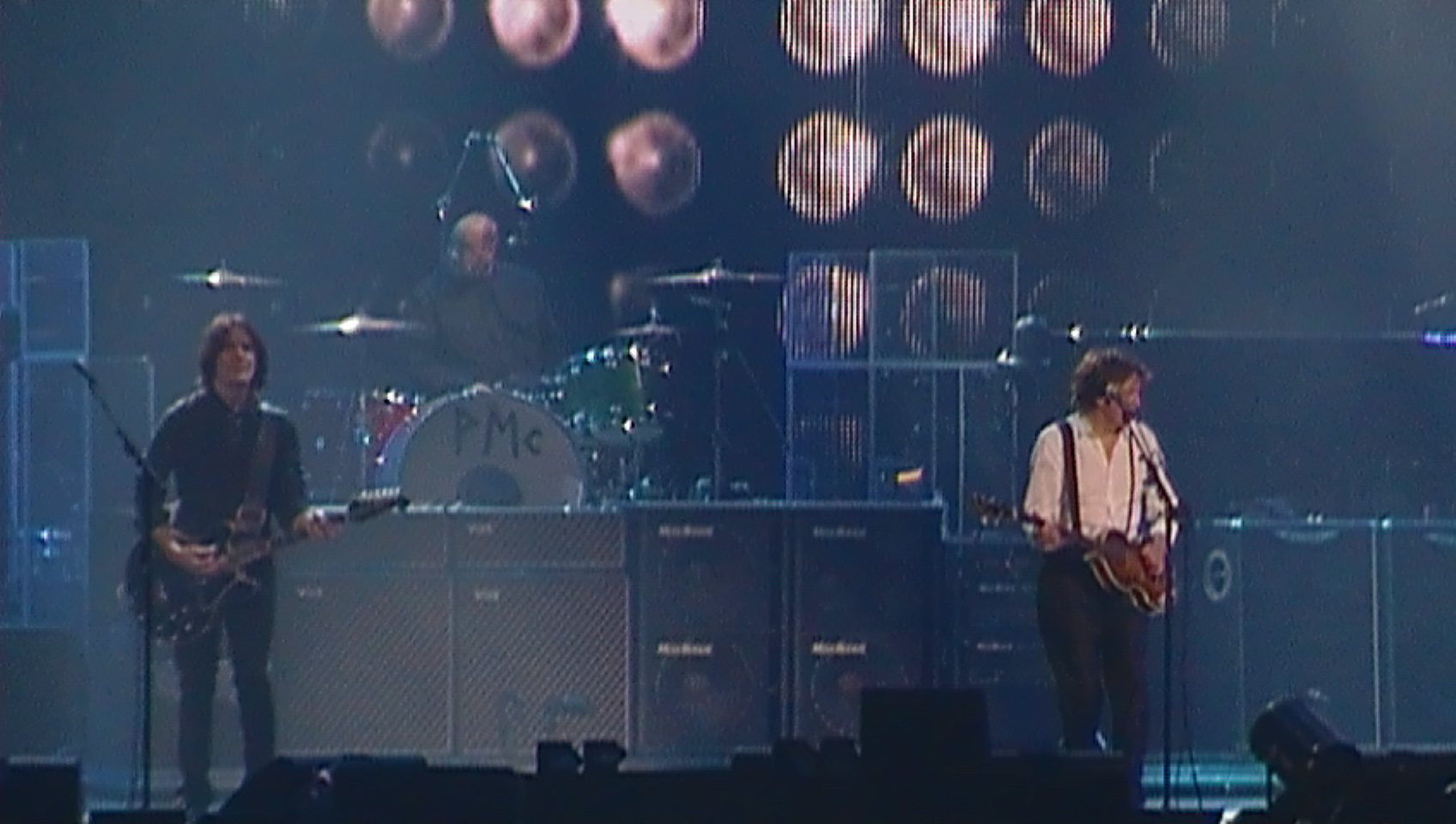 Rusty at left on electric guitar and Paul at right on bass, on a darkened stage, with Abe on drums in the background, for the Montreal 2010 show